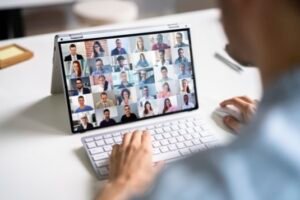 Man facing a laptop screen with many participants. Representing the format of the interactive, virtual EKBN knowledge cafe.